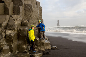 Children, boy brothers, posing on the rock of black sand beach of Reynisfjara and the mount...