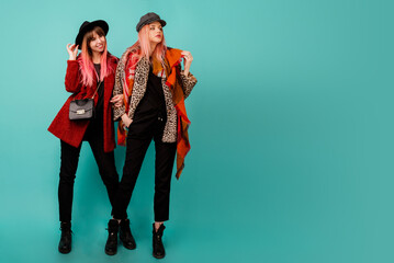 Full height image of two happy cheeky girls , best friends posing  on blue background. Wearing stylish casual   fur coat with leopard print  and hat. Space for text.