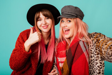 Close up studio portrait of two pretty cute models with pink hairs in stylish leopard print faux fur coat and trendy hat on turquoise. Surprise face. Winter fashionable outfit.