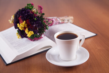 Colorful flowers and a cup of coffee with a book on a wooden background.