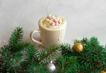 Celebrating Christmas. Hot Christmas drink. A cup of hot chocolate with marshmallows on a white marble background, branches of a Christmas tree, decorations and balls. View from above
