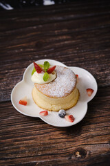 Fluffy souffle pancakes with cream and berries on white plate set on wooden table.