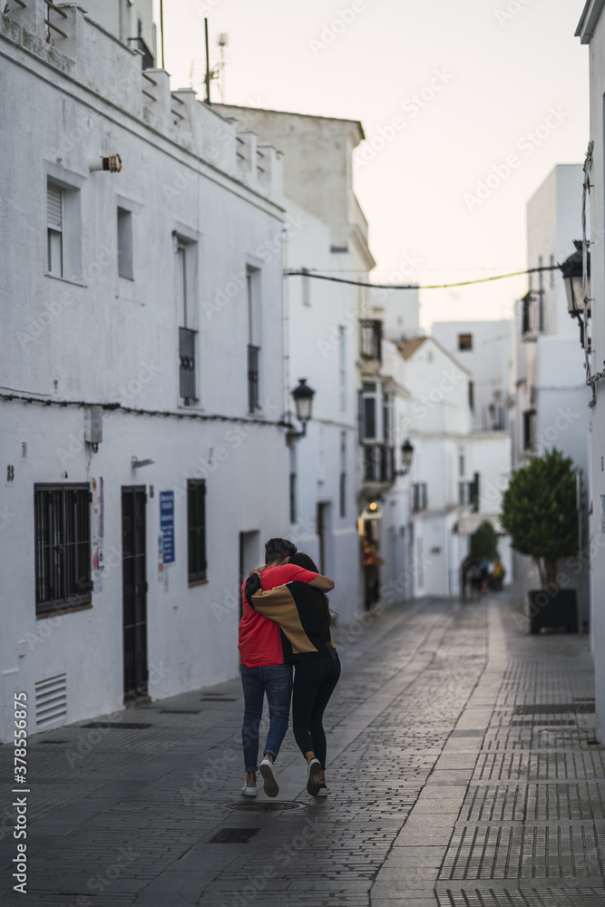 Poster Young couple holding hands walking through white town