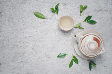 Tea concept with Creamy white tea set of cups and teapot surrounded with equipment and fresh tea leaves on concrete background with copy space.