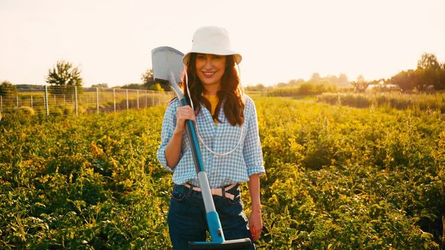 woman in hat holding shovel and standing in field 