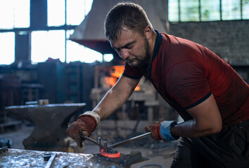 The blacksmith bends the red-hot metal product with his hands