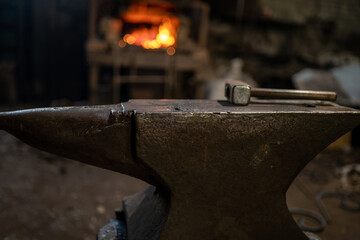 A blacksmith's hammer lies on an anvil against the background of a burning forge