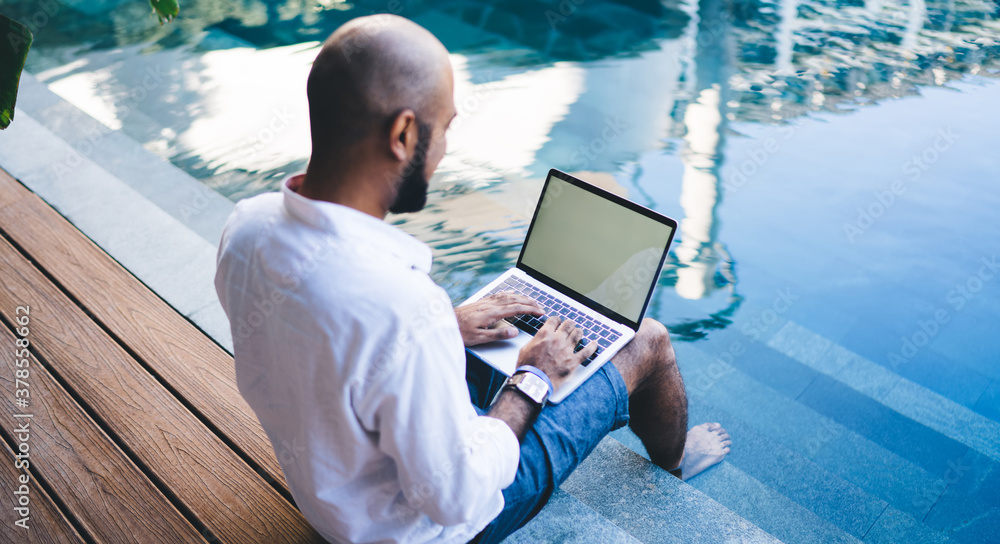 Aufkleber skilled digital nomad user sitting at pool terrace in courtyard of own indonesian villa and typing c