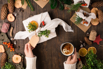 Woman is wrapping gifts in linen fabric on dark rustic wooden background.