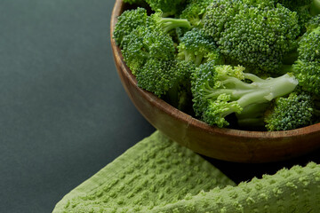 Fresh Broccoli in wooden bowl and seed oil in rustic style. Close up on a black background. side view, harvest cruciferous copy space for text.