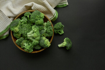 Fresh Broccoli in wooden bowl and seed oil in rustic style. Close up on a black background. copy space for text. Top view, flat lay.