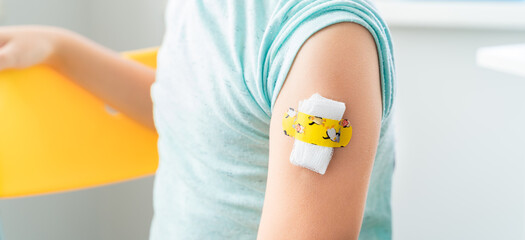 Vaccination of little girl in doctor's office.Kids funny adhesive plaster,gauze napkin.Sits on chair.Vaccine for covid-19 coronavirus,flu,infectious diseases.Injection.Clinical trials for human,child