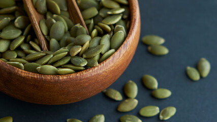 pumpkin seeds in a wooden bowl and vintage scoop. Close up on a black background. copy space for text