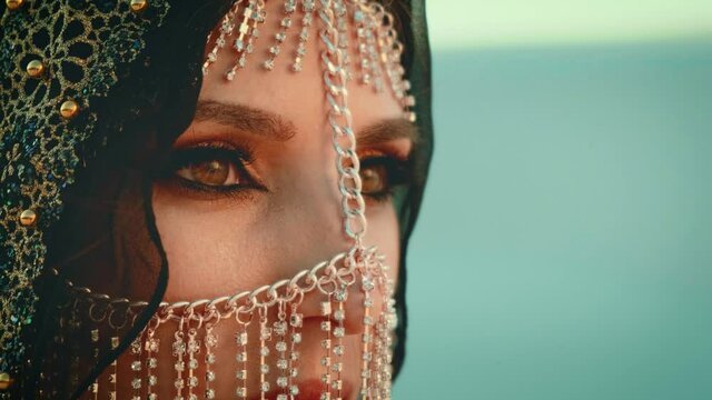 Close-up portrait of a yong arabian woman. Beautiful brown eyes with oriental makeup. Gold accessories, the mask hides the face.
