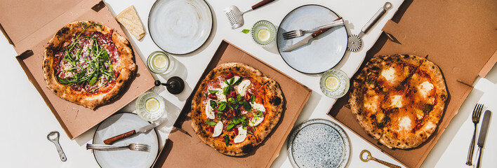 Pizza party for friends or family. Flat-lay of pizzas in boxes, lemon drinks and cutlery over plain white table background, top view. Fast food, comfort food, Italian cuisine concept