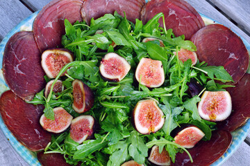 Platter with bresaola dried beef, arugula salad and fresh figs