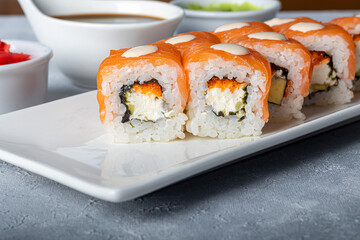 Sushi Sets Nigiri, Uramaki, California, Philadelphia, on a white plate. Nearby ginger and wasabi. Soy sauce in a white bowl. On a light gray background.