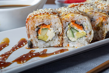 Sushi Sets Nigiri, Uramaki, California, Philadelphia, on a white plate. Nearby ginger and wasabi. Soy sauce in a white bowl. On a light gray background.