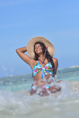 Hispanic woman with straw hat siting on shore beach laughing with close eyes and splash water. Happiness fantasy Concept