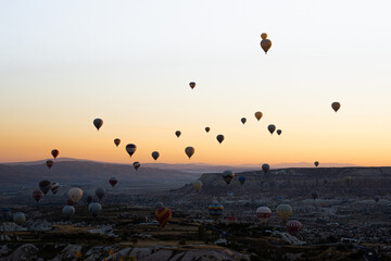 Colorful hot air balloons flying over Goreme National Park mountains at sunrise, Cappadocia, Turkey.