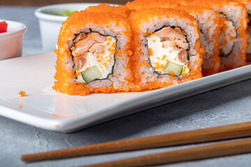 Sushi Sets Nigiri, Uramaki, California, Philadelphia, on a white plate. Nearby ginger and wasabi. Soy sauce in a white bowl. On a light gray background.