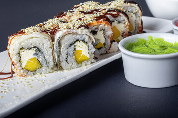 Sushi Sets Uramaki, California, Philadelphia, on a white plate. Nearby ginger and wasabi. Soy sauce in a white bowl. On a dark background.