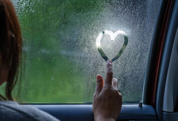 Side view of romantic woman drawing heart on steamy car window