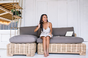 Joyful young ethnic female laughing while resting on couch