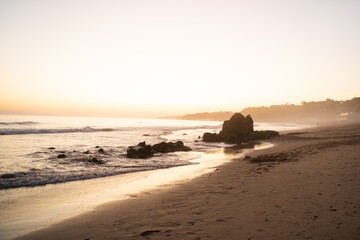 Rocks on Falesia Beach with golden sand and fog at sunset on the Atlantic Ocean. Olhos de Agua, Algarve, Portugal.