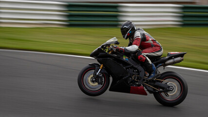 A panning shot of a racing bike on one wheel as it circuits a track.