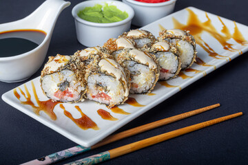 Sushi Sets Uramaki, California, Philadelphia, on a white plate. Nearby ginger and wasabi. Soy sauce in a white bowl. On a dark background.