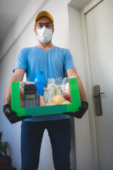 Fototapeta na wymiar Delivery guy with protective mask holding box / bag with groceries and POS for contactless payment.