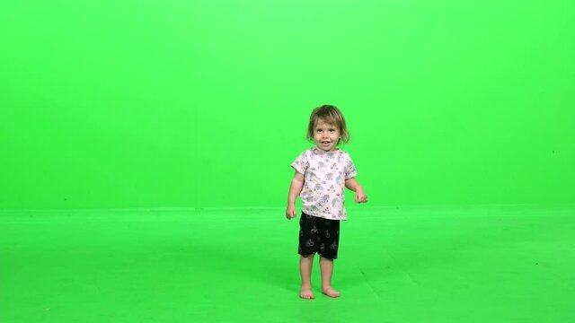 Happy toddler girl smiling and trying to dance, going around in circles and giggling over green screen.