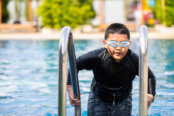 Fat asian boy in swimsuit and goggles swimming in the pool