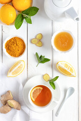 Antioxidant healthy tea with lemon, ginger, honey, turmeric and mint on a white wooden table.