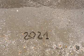 New Year 2021 is coming - inscription 2021 beach sand the wave water is starting to cover the digits - Summer beach holiday 2021 season golden sand old year - message handwritten - empty copy space
