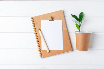 Desktop mockup planner. Flat lay of white wooden table background. Top view green sprout leaves, coffee cup, blank, craft Notebook. Zero waste, eco friendly, natural organic concept