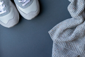 Light gray suede and mesh walking shoes, sneakers and a warm knitted sweater on a gray paper background