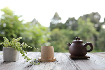 Traditional clay tea pot with bamboo wooden cup and New Large Pearl Grass plant on wooden table