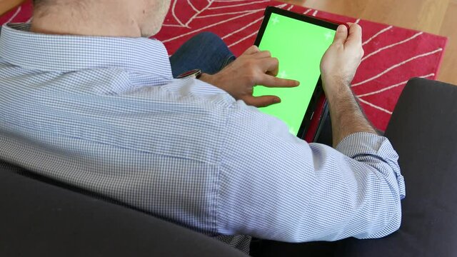Man looks at the tablet sitting on the sofa and scrolls images from right to left, tablet with chromascreen