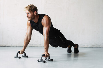 Photo of athletic young sportsman working out with push-up stops