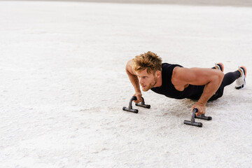 Photo of athletic young sportsman working out with push-up stops