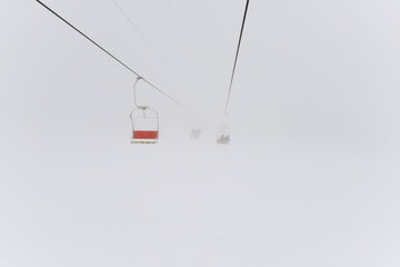 Empty ski lift chair during a snow storm. Gray haze and chair lifts in the fog. Lack of tourists...