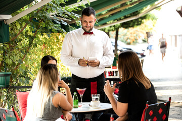 A young waiter serves a drink in the garden of the cafe restaurant
