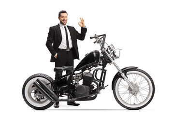 Man in a black suit standing with a chopper motorbike and gesturing ok sign