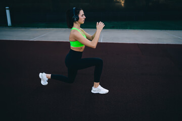 Slim Caucasian girl in bluetooth headphones keeping perfect body shape training legs enjoying...