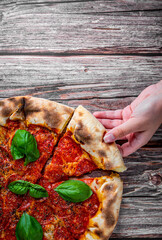 woman Hand takes a slice of Pepperoni Pizza with Mozzarella cheese, salami, Tomatoes, pepper, Spices and Fresh Basil. Italian pizza on wooden table background