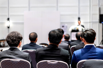 Backside of three Asian business men sit and listended speaker on the podium in front of the conference room.
