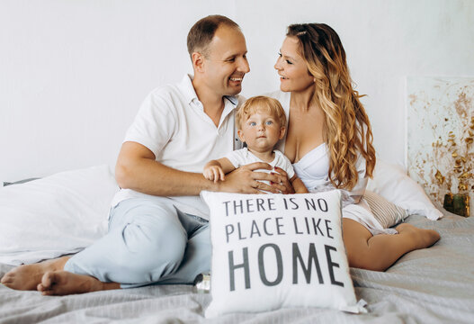 Happy Family Mom, Dad And Son Sitting At Home On The Bed.