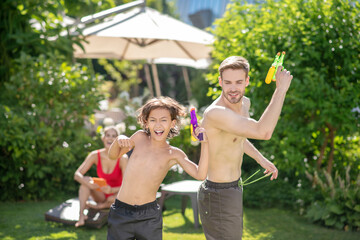 Fototapeta premium Fun dad and son with water pistols mom behind